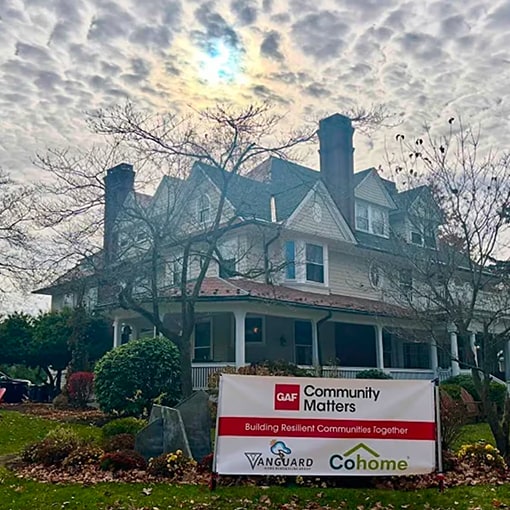 Renovated Victorian home with a GAF Community Matters and Cohome project banner on the front lawn.