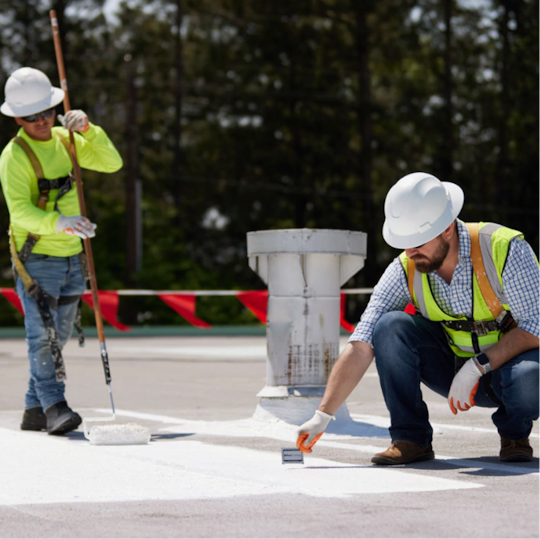 Two GAF certified professionals in safety vests standing on a white roof, collaborating.