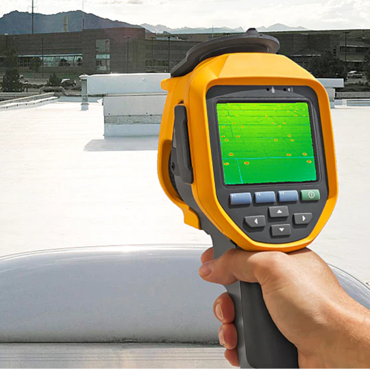 A handheld thermal camera scanning a commercial roof surface to evaluate heat loss around fasteners.