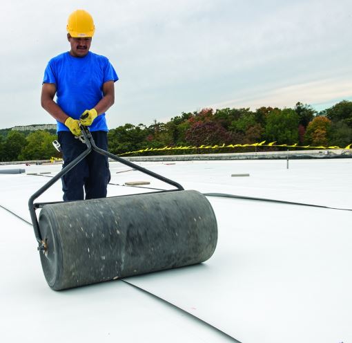 roofer rolling pvc membrane over a roof deck