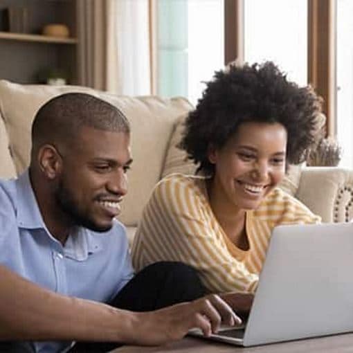 Man and woman smiling while reviewing items on a laptop.
