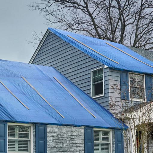 Blue tarp covering the missing roof of a gray house after a storm