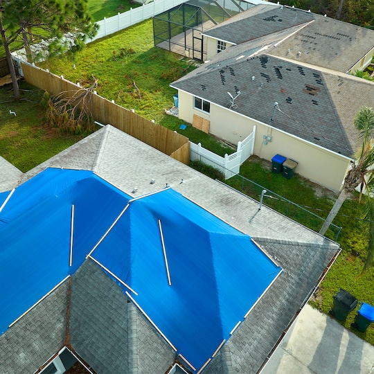 Bird’s eye view of a house with blue tarps covering its storm-damaged roof. 