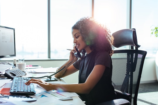 Women on phone at desk typing on a computer keyboard