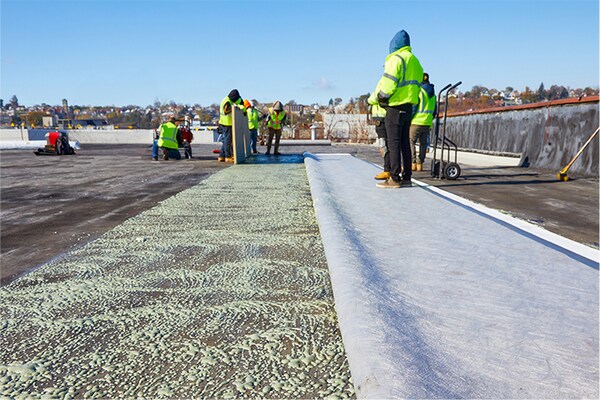 A worker unrolling a textured fleece-backed roofing sheet on a large commercial roof.