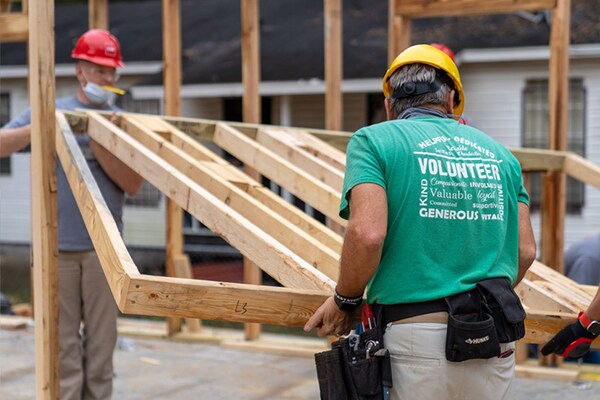 Volunteer contractors lift a wooden house frame together.