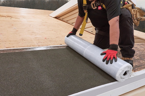 A contractor installs a leak barrier on a roof.