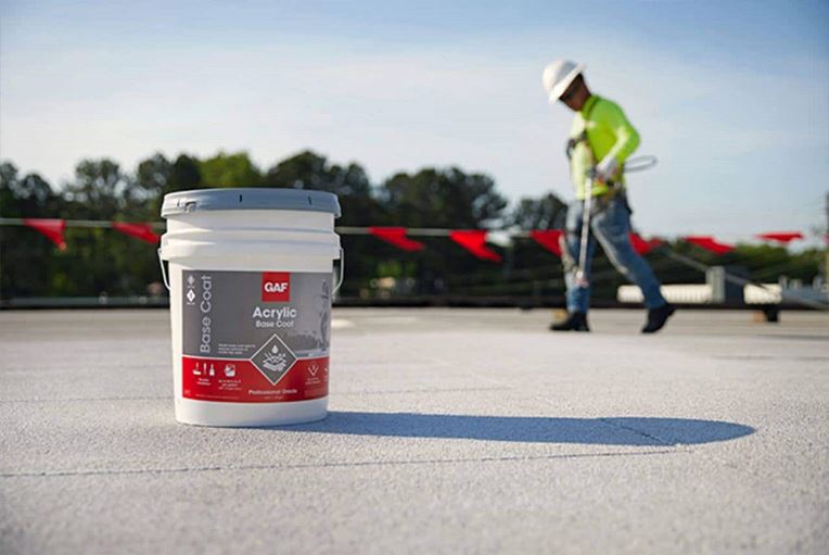 A contractor applying GAF acrylic top coat on a flat roof.