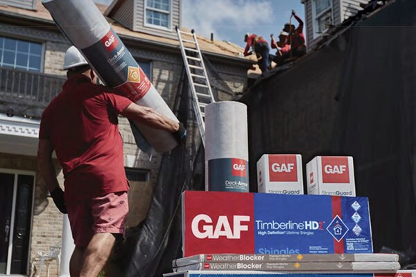 GAF residential roofing materials outside home with roofer holding rolled product