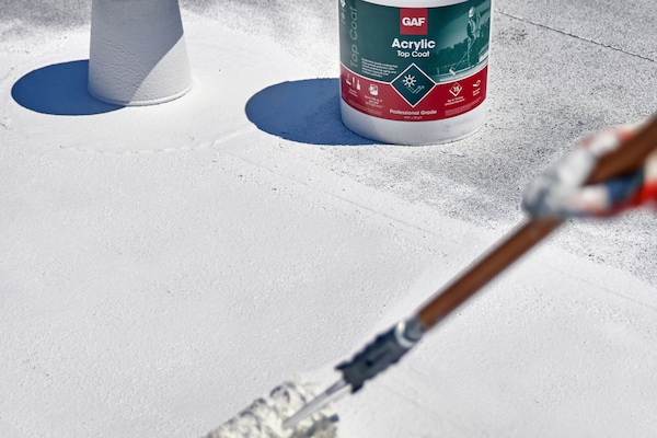 A contractor applying GAF Acrylic Coat Top Coat on a flat roof.