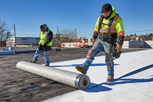 Two commercial roofing employees rolling single-ply membrane on a flat rooftop.