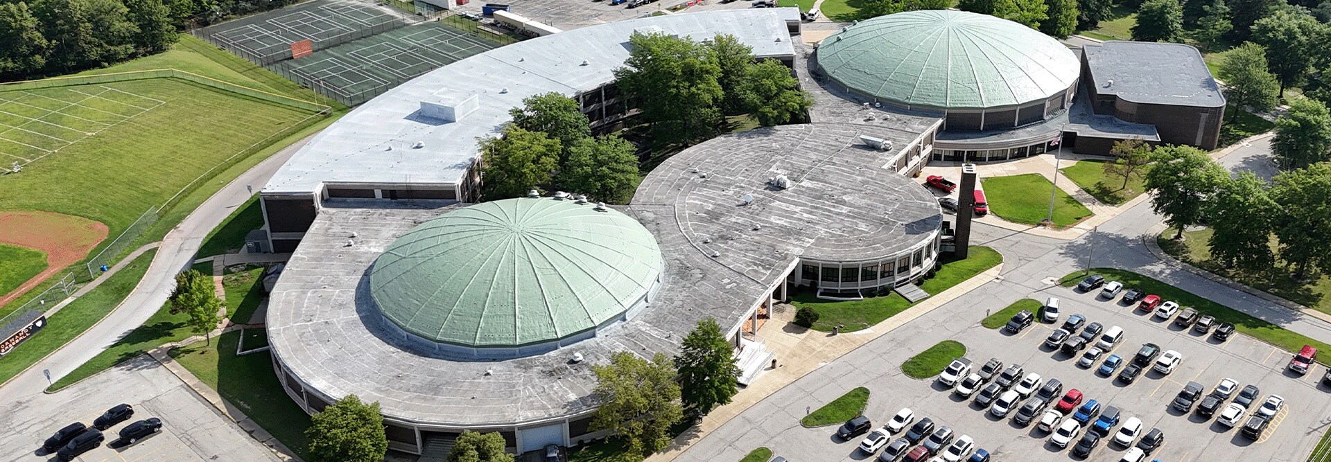 Aerial view of Normandy High School in Parma, Ohio showing worn Patina Green domes and classroom wing roofs before GAF silicone coating restoration