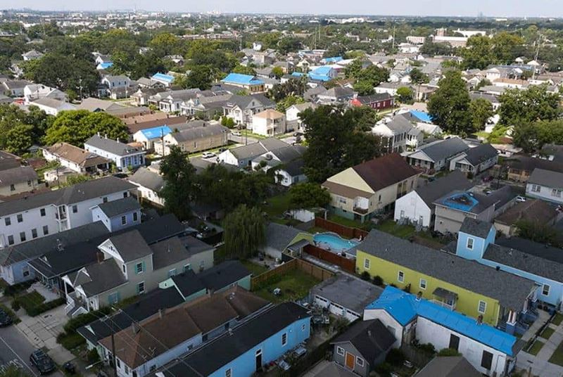 Aerial view of neighborhood with many houses that have blue tarps over missing roofs