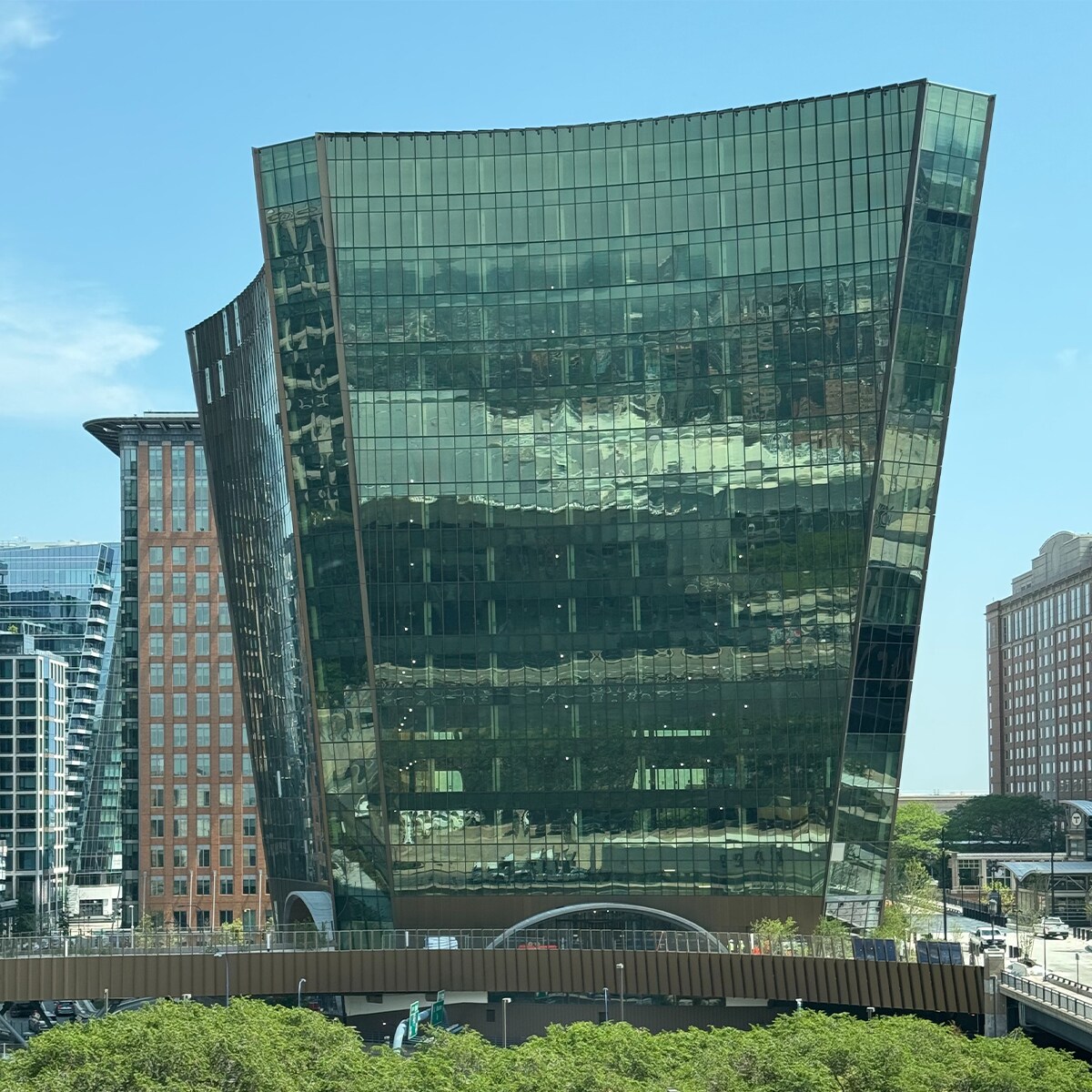 Curved 10 world trade building reflecting sky and clouds, surrounded by modern and traditional architecture; bright, clear day.