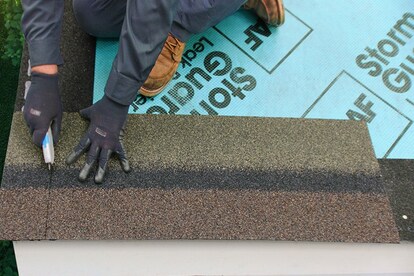 Roofing worker using a utility knife to trim 5 inches from the rake edge of a starter strip shingle.