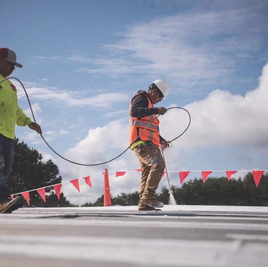 roofer spraying roof coating over a low-slope roof deck