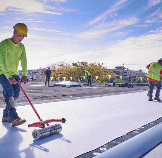roofer spreading out tpo membrane over roof deck