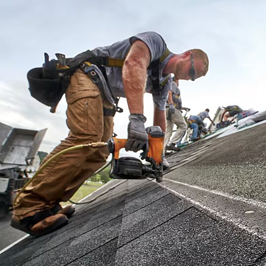 A man with ha nail gun installs shingles