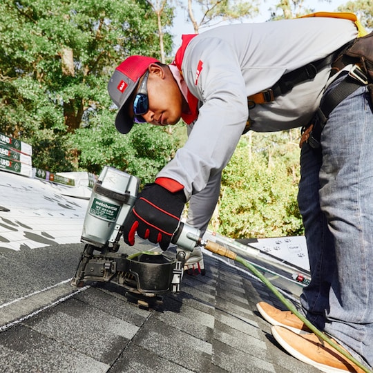 A roofer uses a nail gun to secure shingles on a roof. 