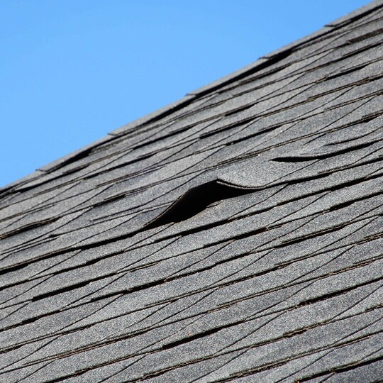 Aged shingles on a roof, showing a gap where leaks can come from. 