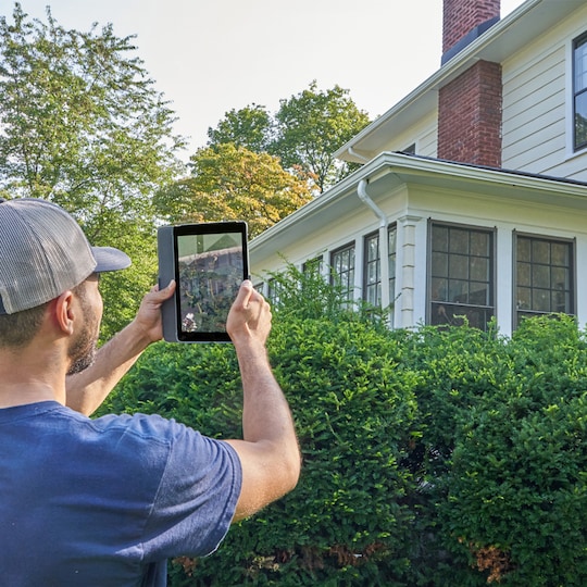 Roofing contractor holding tablet up in front of home to review roof documents