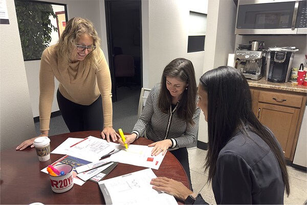 Three members of the GAF Building & Roofing Science team collaborating over project documents at a table in an office setting.