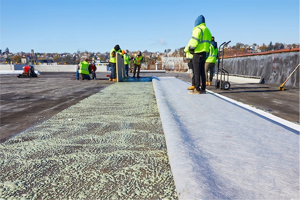 A worker unrolling a textured fleece-backed roofing sheet on a large commercial roof.
