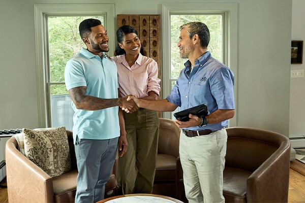 A couple discusses roofing options  with a contractor in front of armchairs at home.