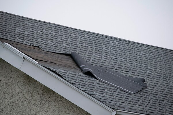 A section of damaged asphalt shingles peeling away from a residential roof.