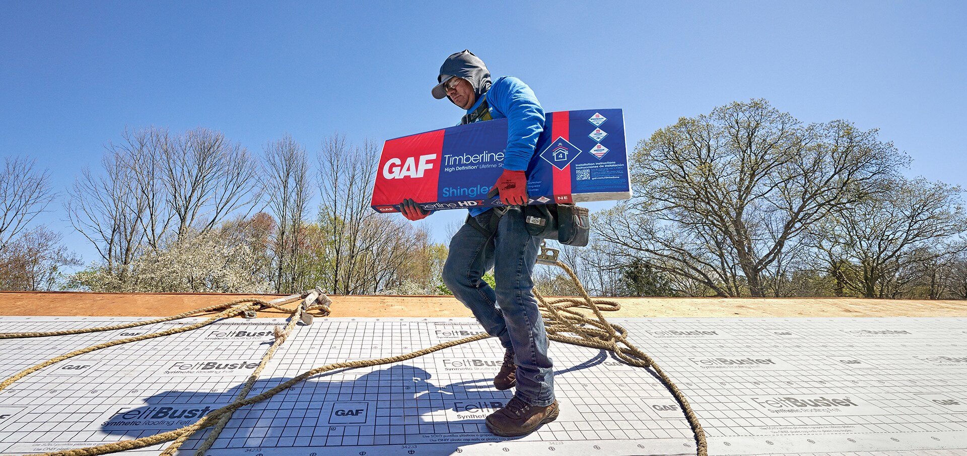 A contractor on a roof holding a package of Timberline HDZ shingles