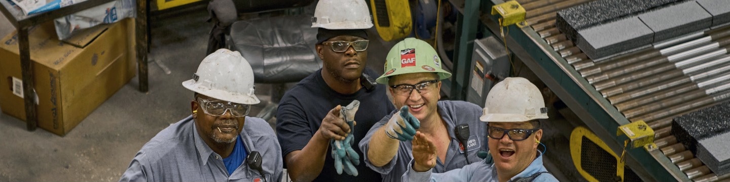 Four excited GAF employees in manufacturing plant 