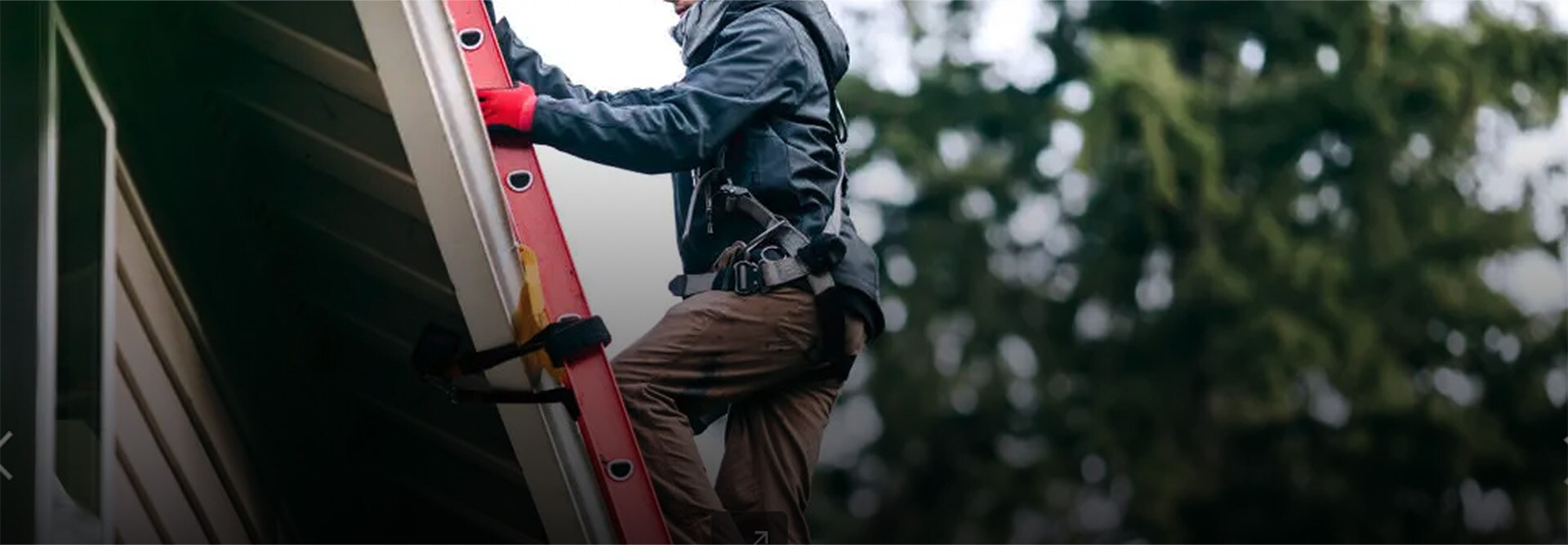 A close-up shot of a GAF certified contractor in full safety gear climbing a ladder to perform a roof repair.