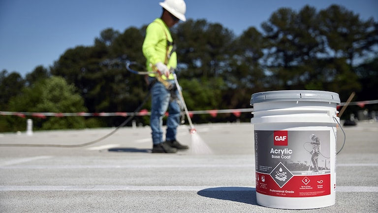Contractor applying GAF Acrylic Base Coat to flat rooftop.