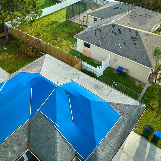 Bird’s eye view of a house with blue tarps covering its storm-damaged roof. 