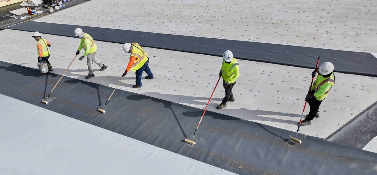 Contractors rolling GAF bonding adhesive onto a flat roof