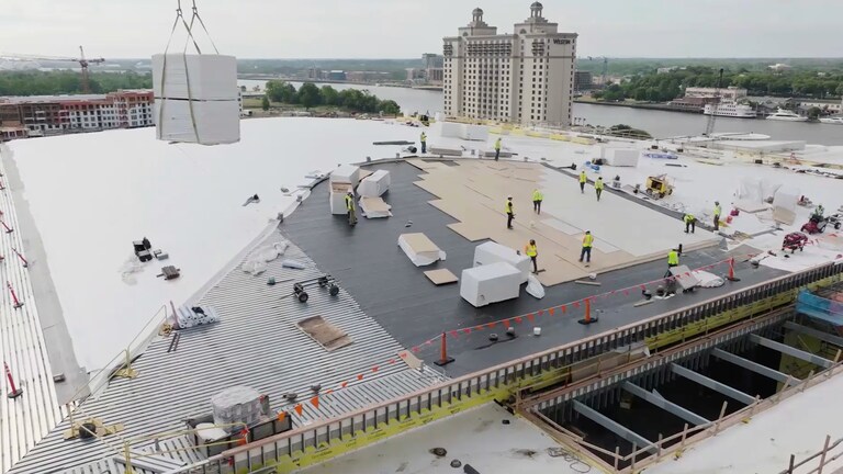 Commercial workers installing roofing materials on a large building with a crane lifting supplies